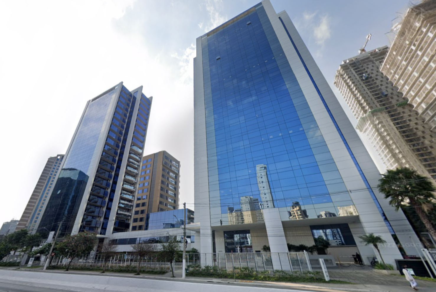 Foto de edifícios comerciais modernos com fachada de vidro azul, em uma avenida urbana com céu parcialmente nublado ao fundo